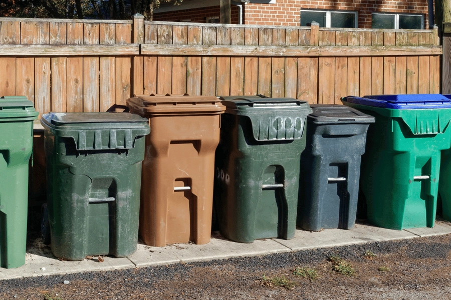 trash and recycling bins lined up along a fence outside